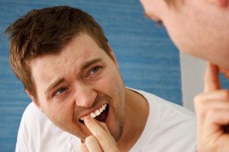 man touching a loose tooth in his mouth while looking in the mirror