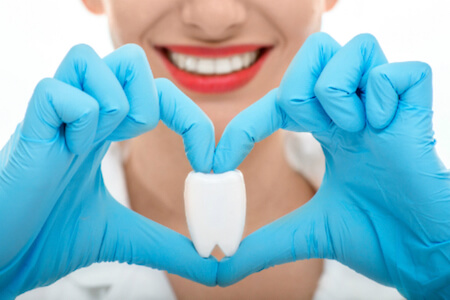 dentist model making a heart shape with her hands while holding a tooth model