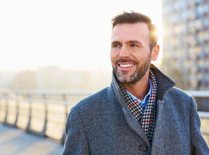 invisalign patient model smiling in a gray coat